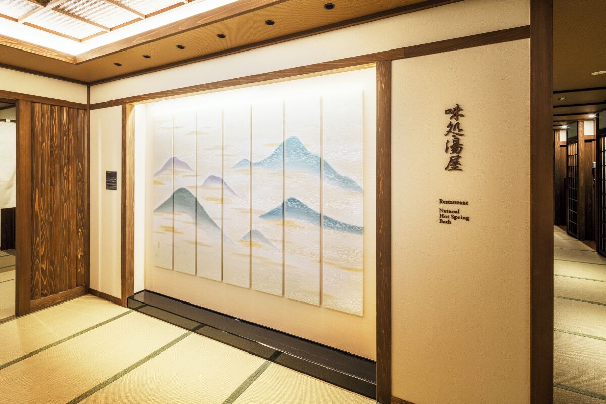 A hallway with tatami flooring, a shoji screen with a mountain landscape, and a sign for a natural hot spring bath restaurant.