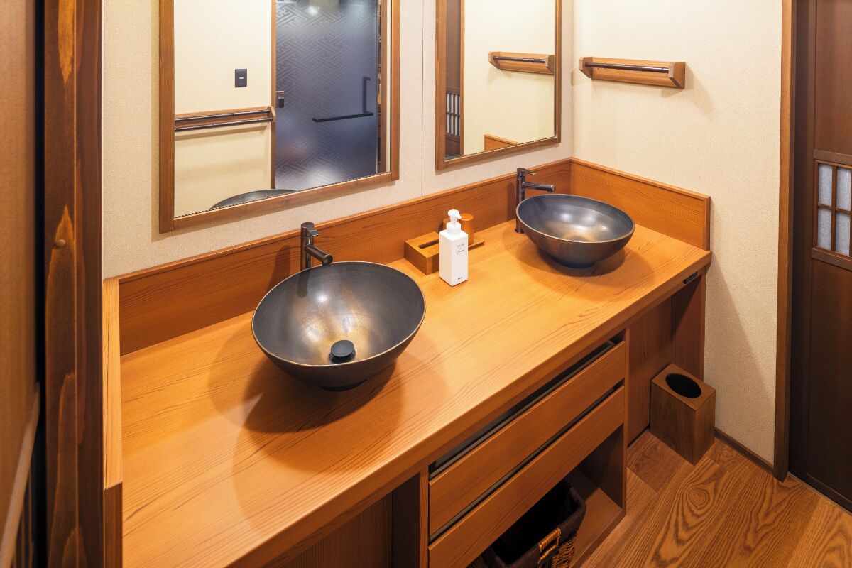 A bathroom with two sinks, wooden vanity, mirrors, and a small trash bin.