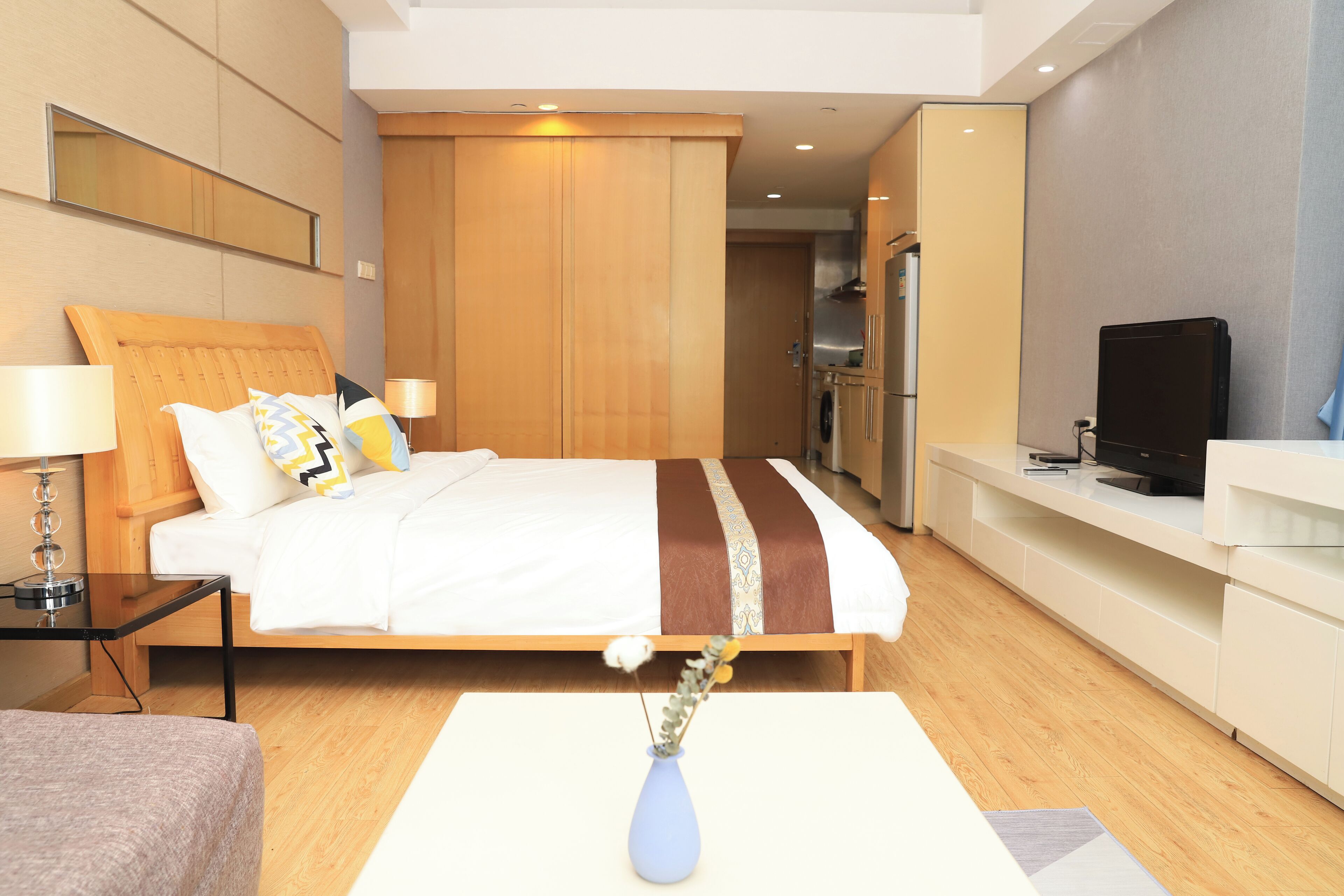 A hotel room with a bed, bedside table, TV, and a vase with flowers.