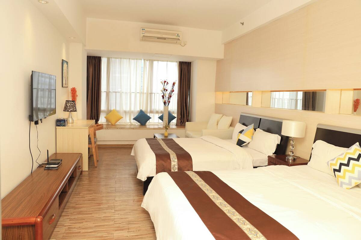 A hotel room with two beds, a desk, a TV, and a window with curtains.