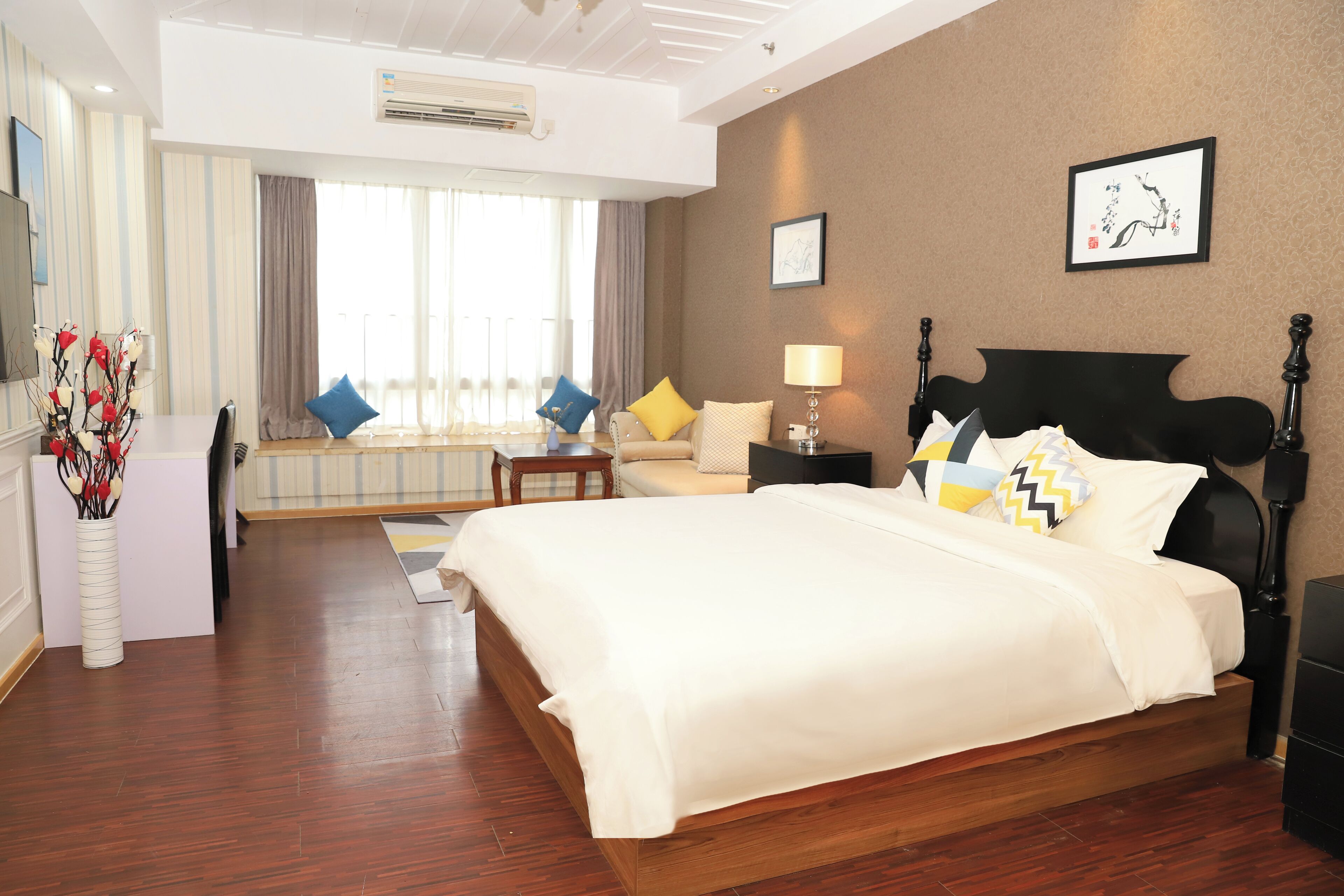 Habitación de hotel con una cama grande, un sofá, una mesita y una ventana con cortinas.