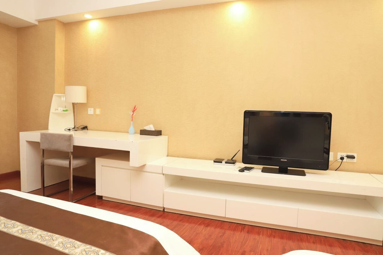 A hotel room with a desk, chair, television, and a small table with a lamp and decorative items.