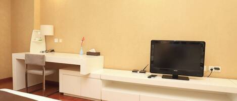 A hotel room with a desk, chair, television, and a small table with a lamp and decorative items.