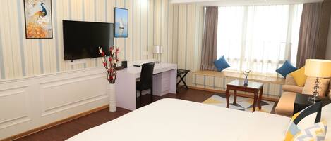 Een hotelkamer met een groot bed, een bureau, een stoel, een televisie en een raam met gordijnen.