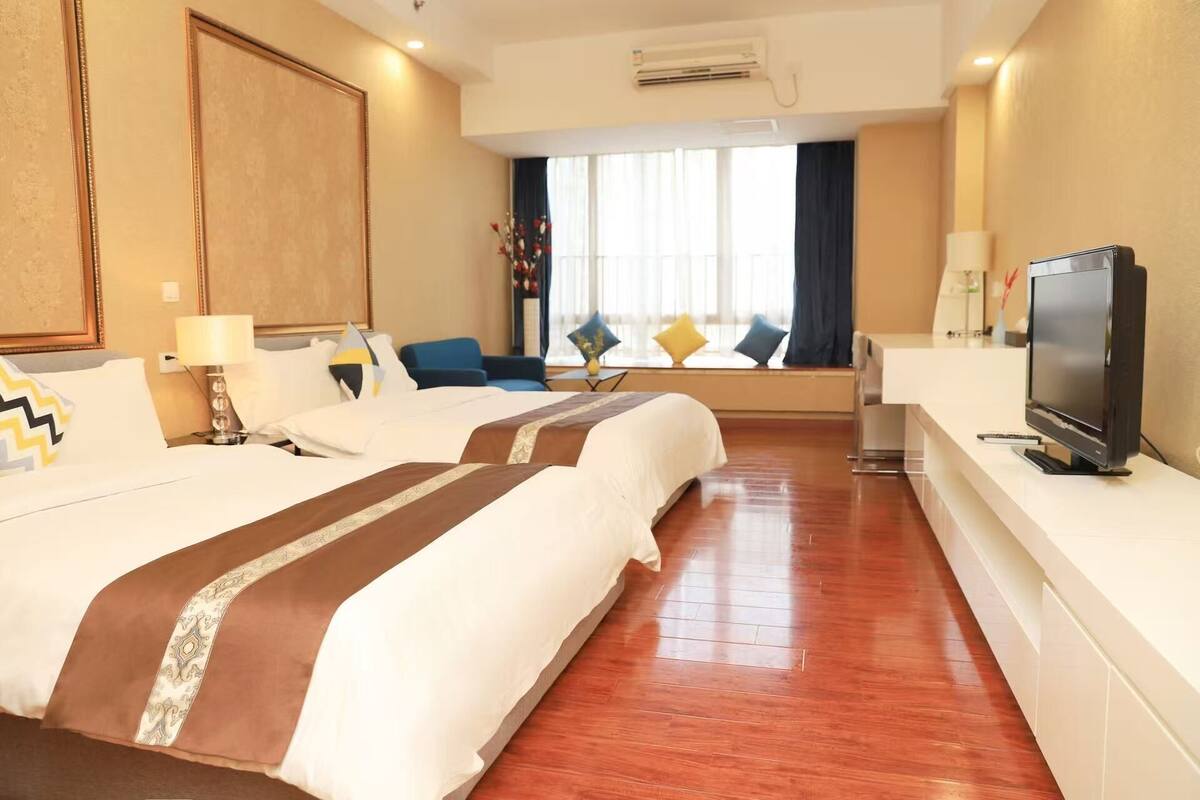 A hotel room with two beds, a TV, a desk, and a window with curtains.