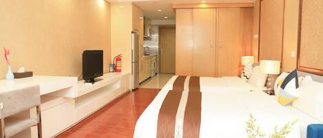 Habitación de hotel con cama, escritorio, televisión, una pequeña mesa con un florero y vistas a la cocina y al baño.