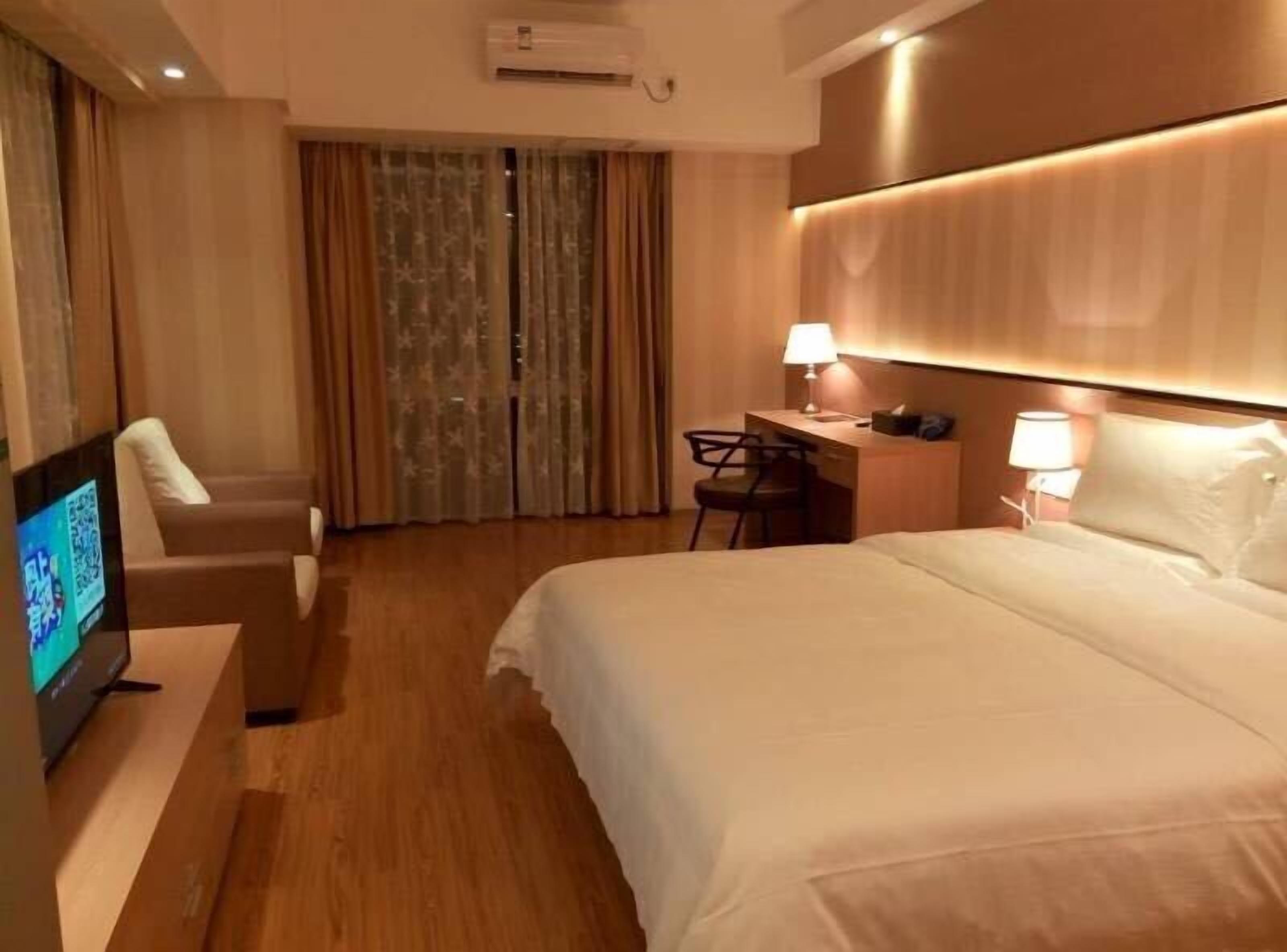 Habitación de hotel con cama, escritorio, silla, televisor y cortinas.