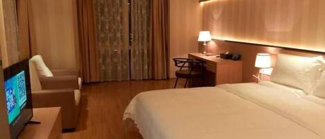 Habitación de hotel con cama, escritorio, silla, televisor y cortinas.