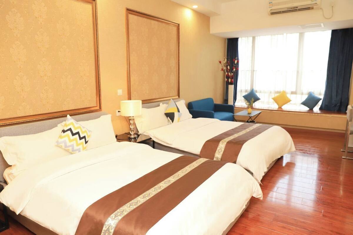 A hotel room with two beds, a sofa, a window with curtains, and a decorative vase.