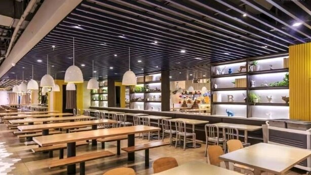 A modern dining area with long tables and chairs, a striped ceiling, and shelves with decorative items.