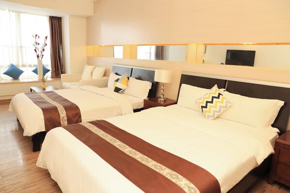 Habitación de hotel con dos camas, un ventanal con cortinas, un jarrón con flores y un televisor de pantalla plana en la pared.