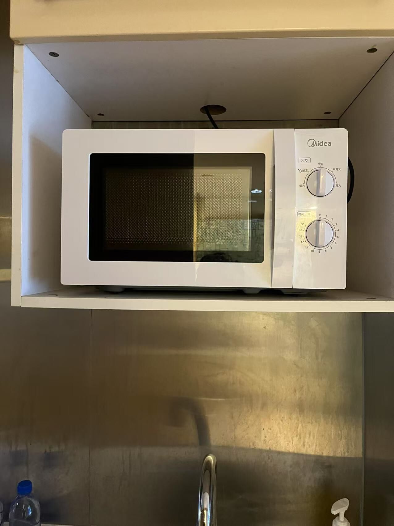 Un horno microondas montado en un estante blanco sobre un lavabo de acero inoxidable.