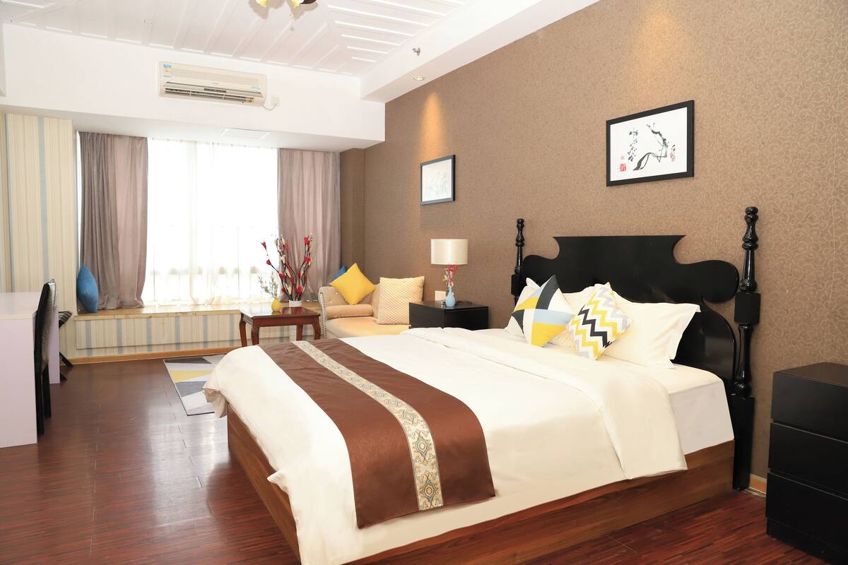 A hotel room with a large bed, bedside tables, a desk, and a window with curtains.