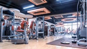 A gym with various exercise machines, a wooden floor, and a ceiling with circular light fixtures.