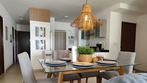 Een moderne eetruimte met een glazen tafel, gestoffeerde grijze stoelen en een hangende rotanlamp.