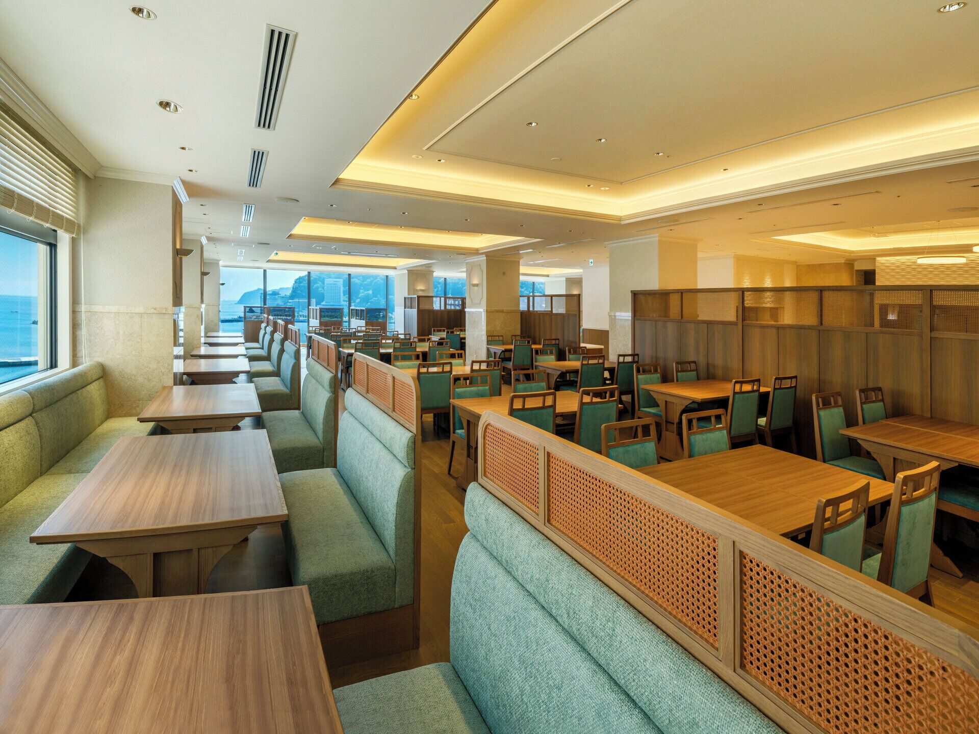 A modern restaurant with high tables and booths, wooden partitions, and a view of the sea.