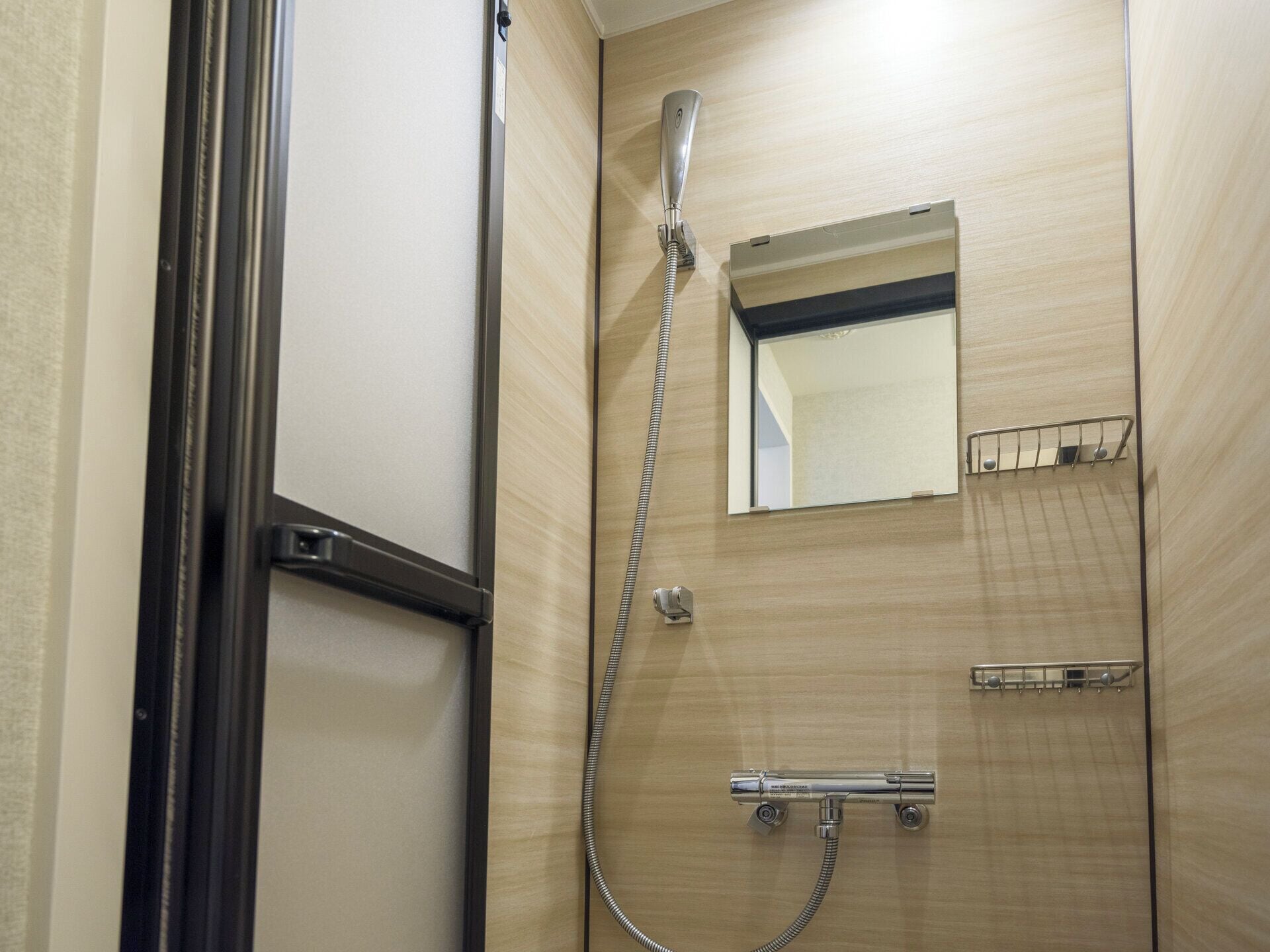 A shower with a handheld showerhead, a wall-mounted mirror, and a towel rack.