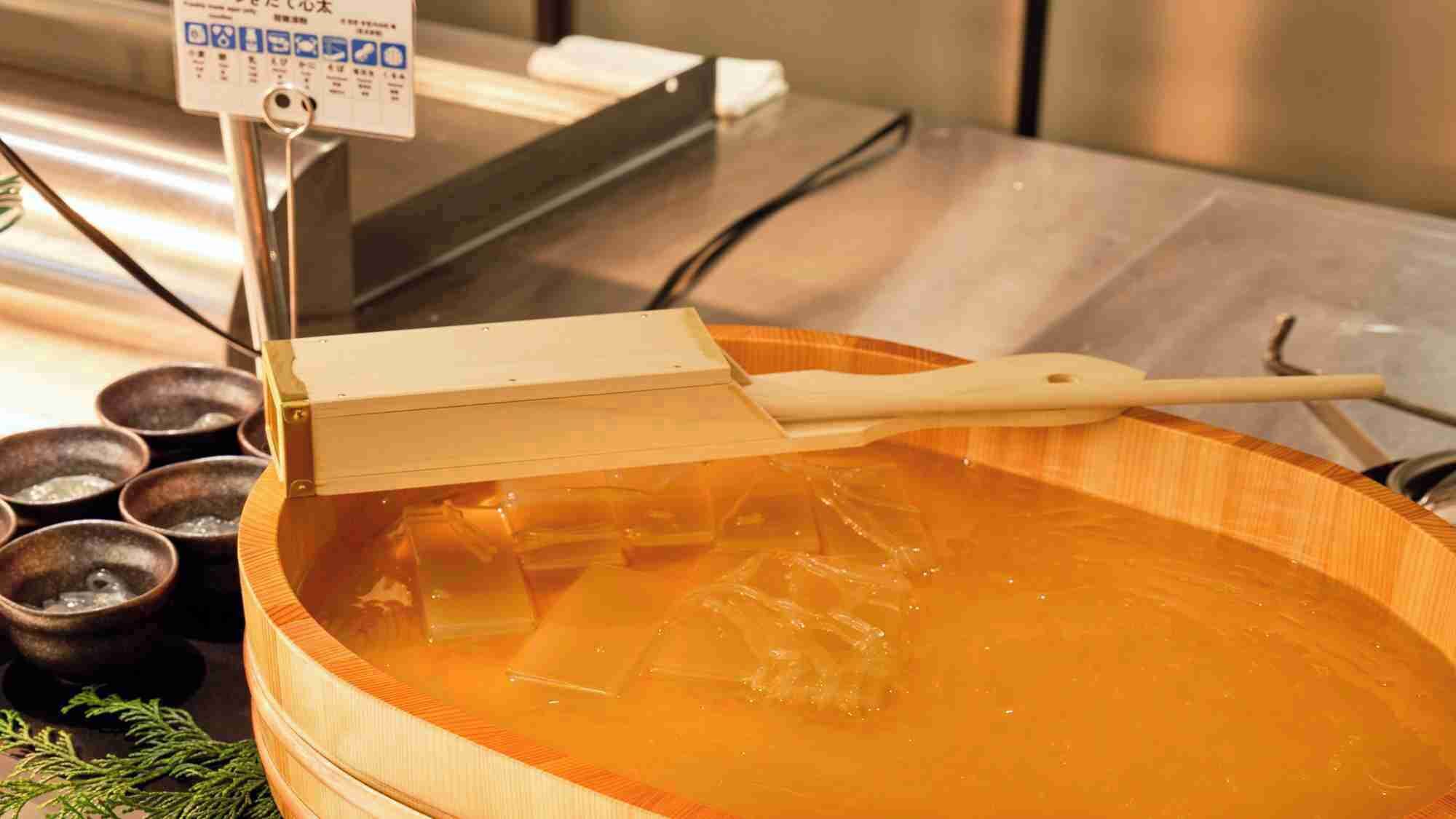 A wooden bowl filled with a clear liquid, possibly a soup or broth, with a wooden ladle resting on top.