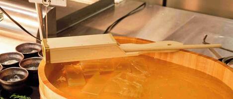 A wooden bowl filled with a clear liquid, possibly a soup or broth, with a wooden ladle resting on top.