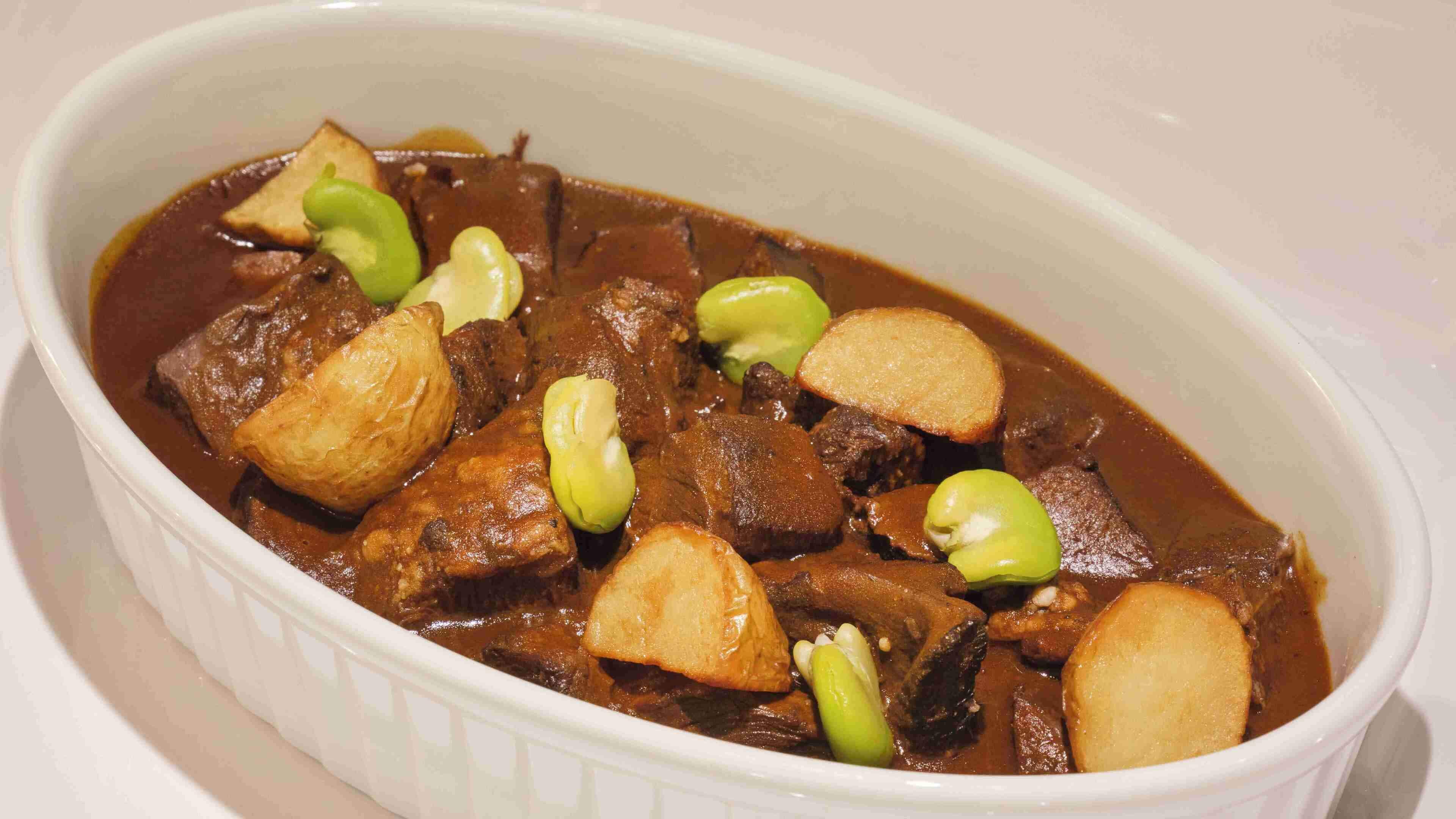 A dish with chunks of meat and potatoes in a brown sauce, garnished with green onions.