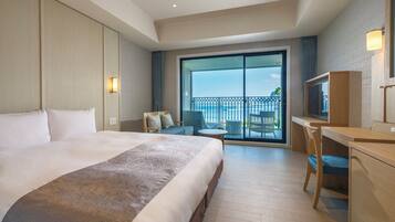 A hotel room with a large bed, a desk, a chair, and a balcony with a view of the sea.