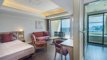 Habitación de hotel con cama, sofá, mesa de comedor y una silla. Tiene un balcón con vistas al mar.