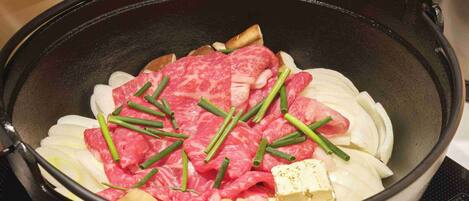 Una olla con carne cruda, cebollines verdes y verduras blancas.