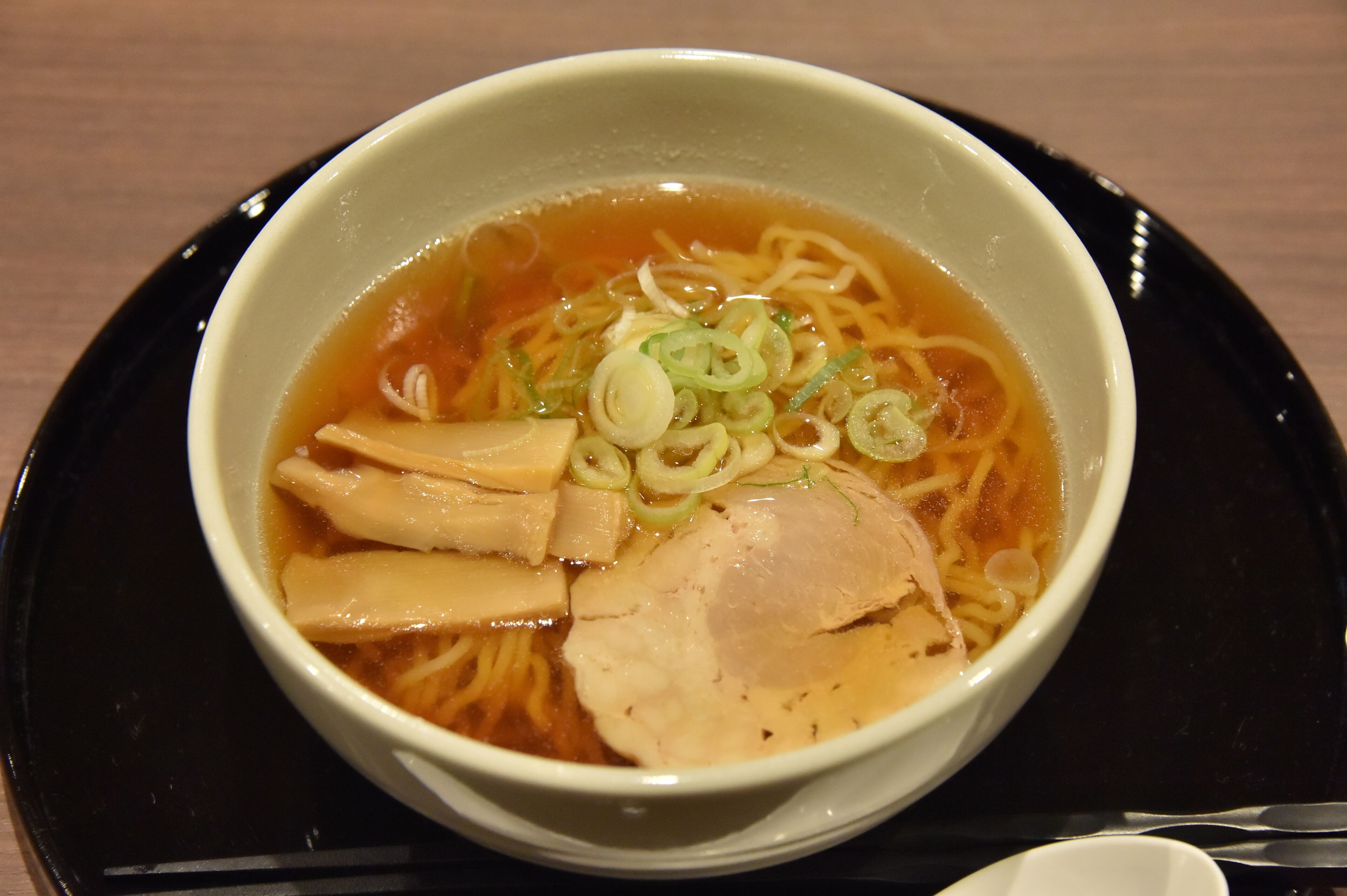 A bowl of ramen with noodles, chicken, and sliced green onions in a broth.