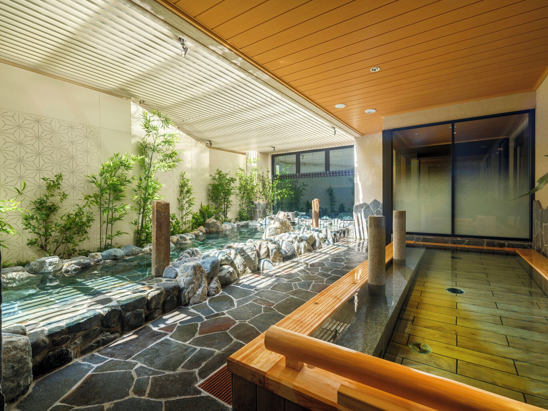 A traditional Japanese onsen with a stone bath, wooden deck, and bamboo plants.