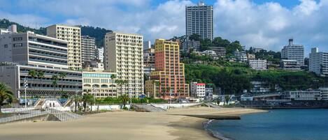 A coastal cityscape with a sandy beach, a variety of multi-story buildings, and a clear blue sky.