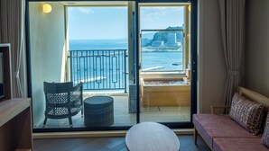 A balcony with a view of the sea and buildings, a sofa, a chair, and a small table. - La Vista Atami Terrace (Atami)