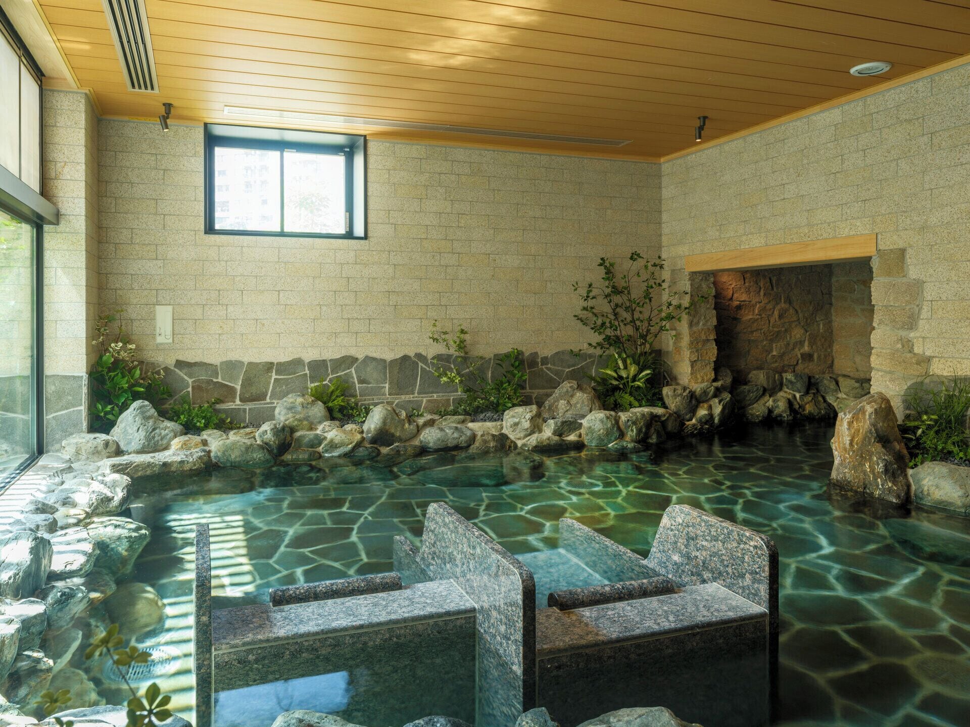 Un espace de détente avec un mur en pierre, une petite cascade et des sièges installés au bord de l’eau.