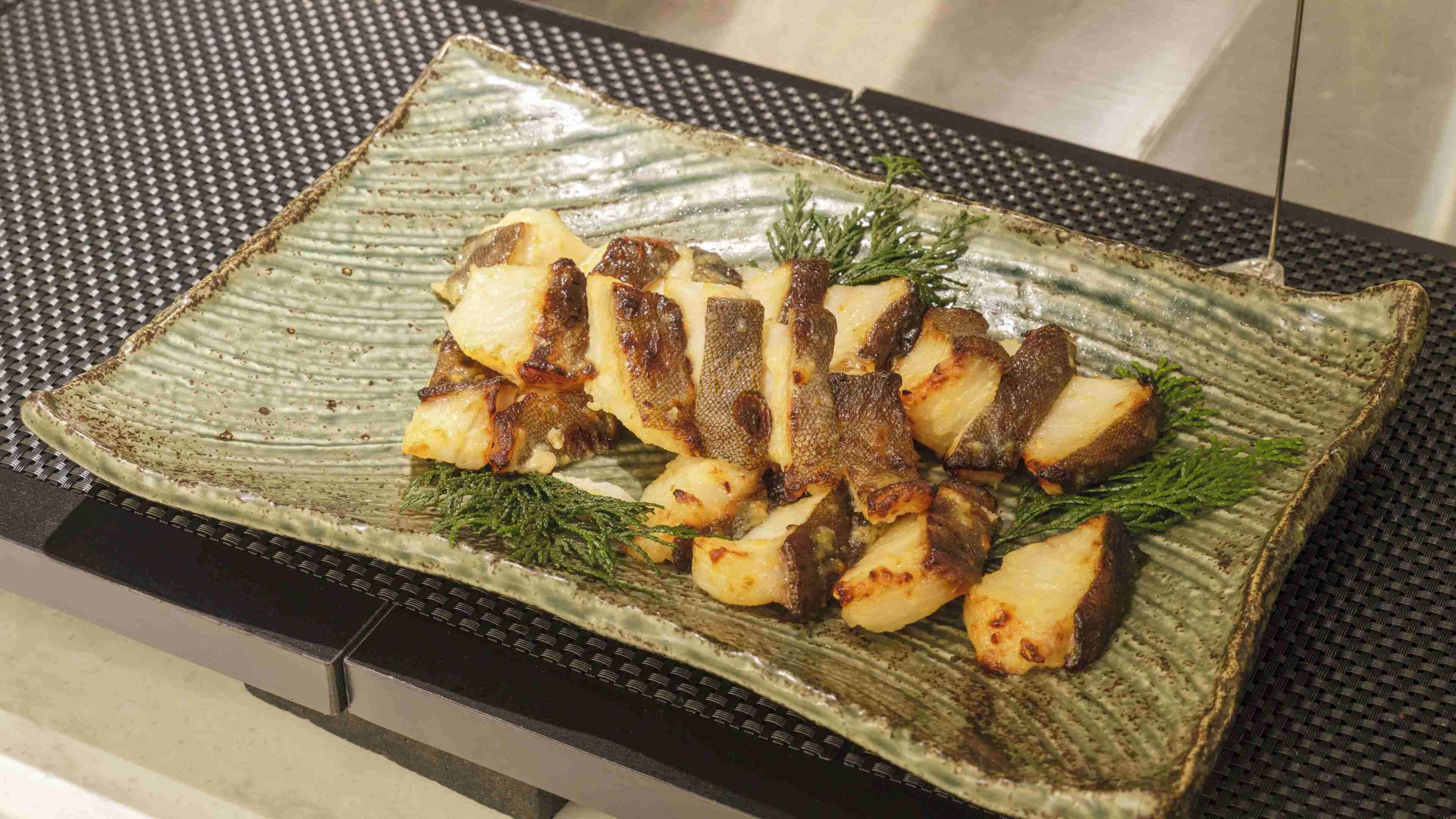 A ceramic plate with roasted fish and herbs on a textured surface.