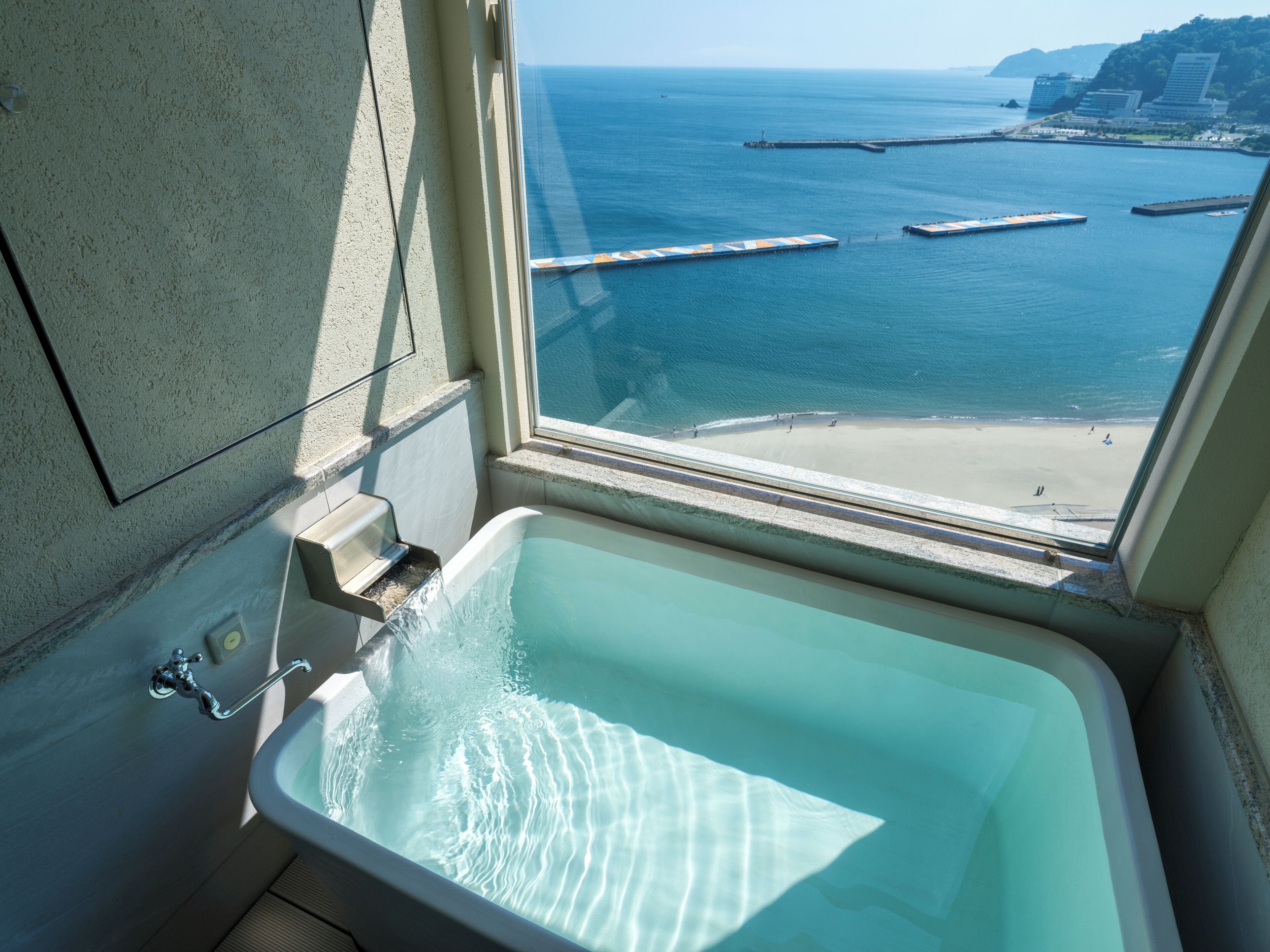 A bathroom with a bathtub and a view of the sea and beach through a window.