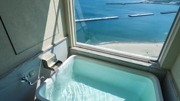 A bathroom with a bathtub and a view of the sea and beach through a window.
