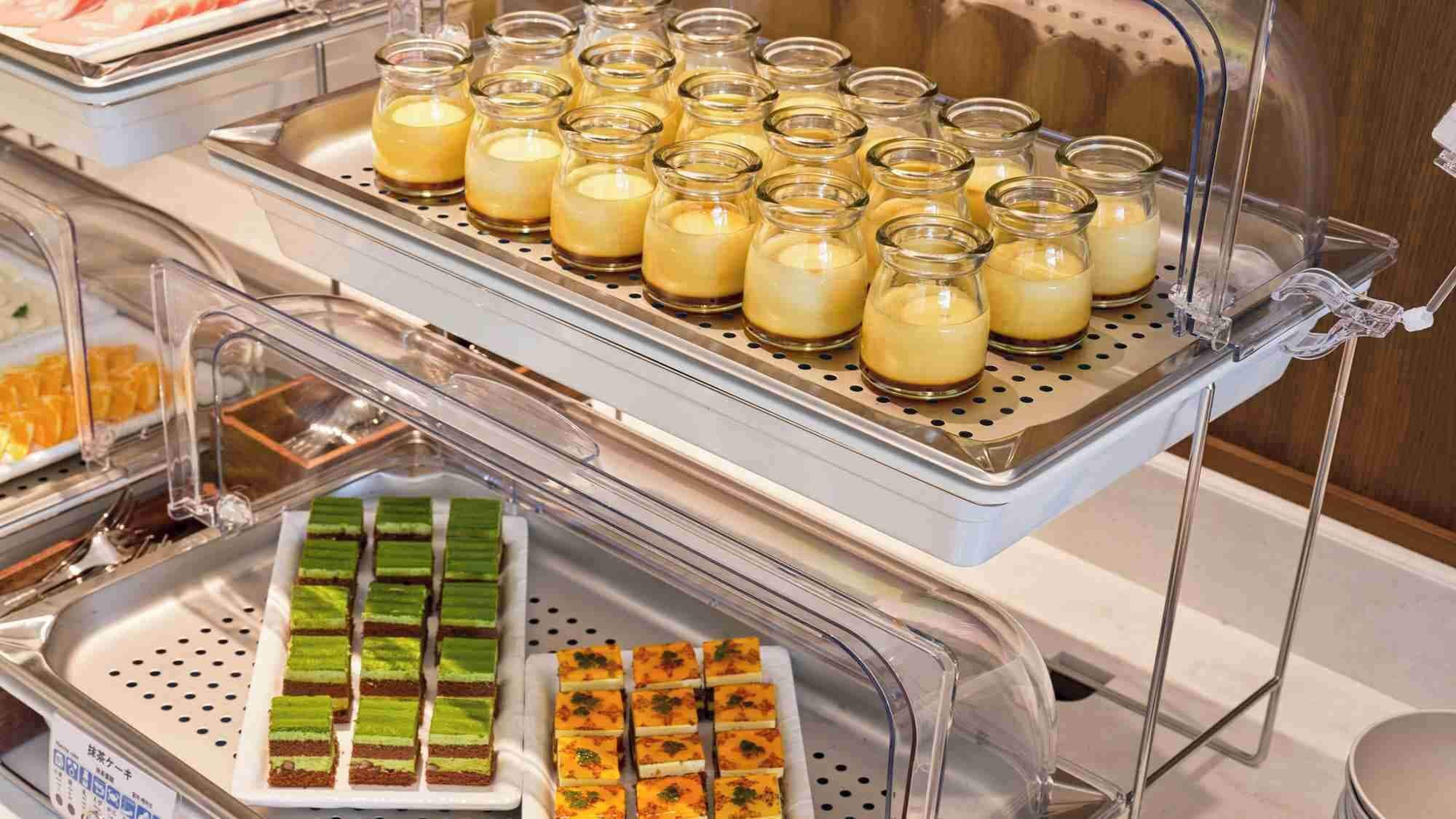 A buffet with various food items including custard in jars, green and orange desserts, and a tray of orange slices.