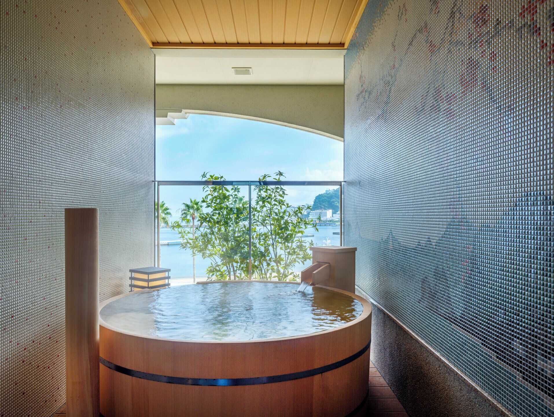 A modern spa with a wooden hot tub, large windows, and a view of the sea.