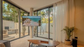A modern living room with a large TV, a coffee table, and a view of a beach through large windows. - Niña Bonita, Tropical Villa 5 min from Tulum beach great location (Tulum)