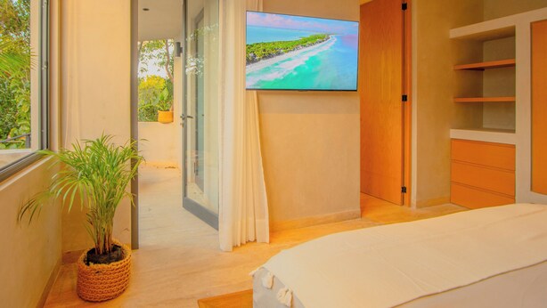 A bedroom with a bed, a TV on the wall, a potted plant, and a view of the outdoors. - Niña Bonita, Tropical Villa 5 min from Tulum beach great location (Tulum)