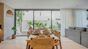 A dining area with a long table set for multiple people, surrounded by chairs with woven seats. - Niña Bonita, Tropical Villa 5 min from Tulum beach great location (Tulum)
