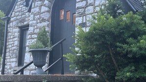 Un edificio de piedra con una puerta oscura, una planta en maceta y una escalera.