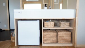 A compact kitchenette with a white refrigerator, wooden shelves, and woven baskets. - JR Mobile Inn Furano (Furano)