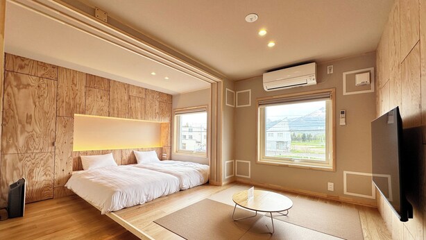 A modern hotel room with a wooden floor, two beds, a small table, and a TV. - JR Mobile Inn Furano (Furano)