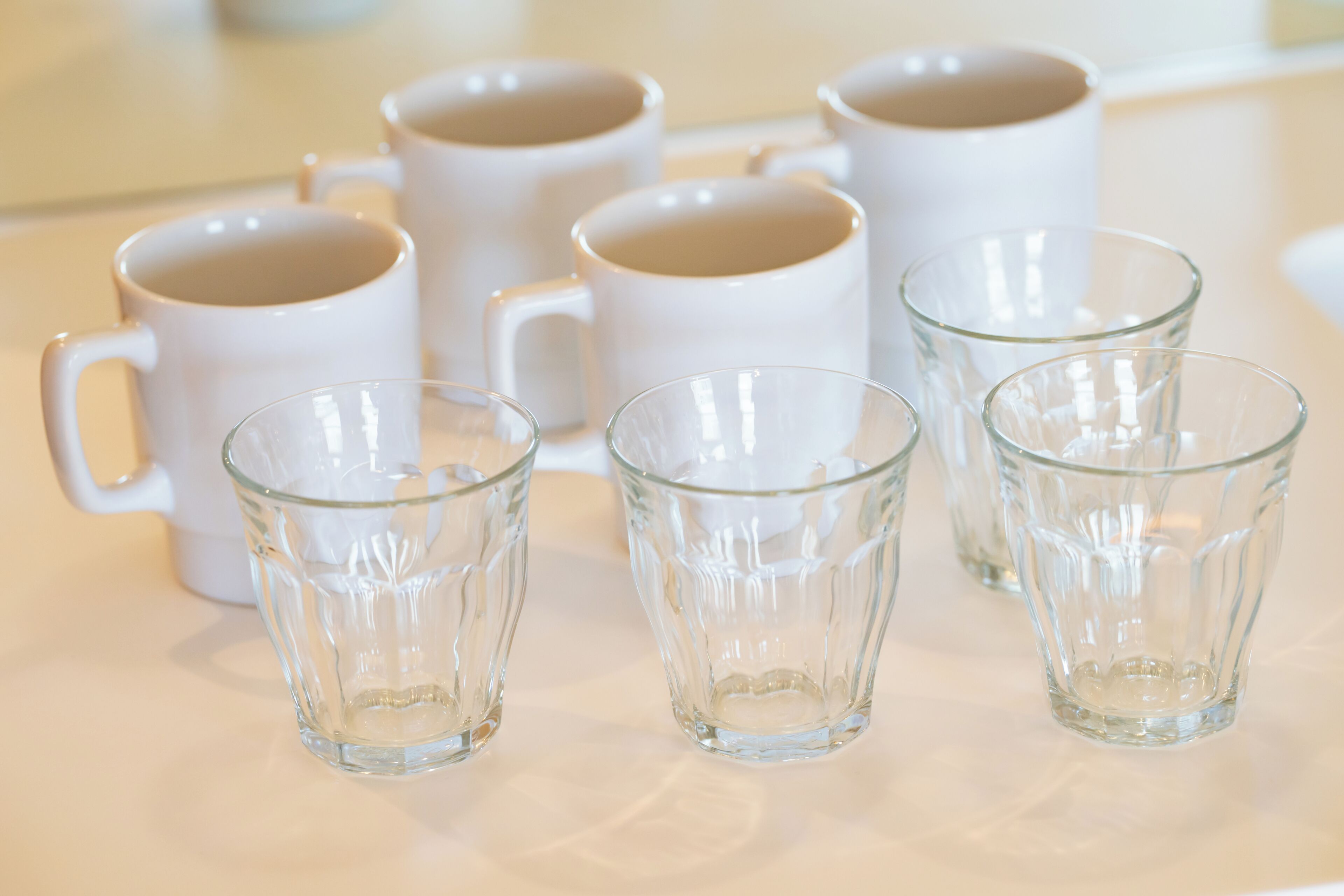 Une table avec six tasses en céramique blanche et quatre verres transparents.