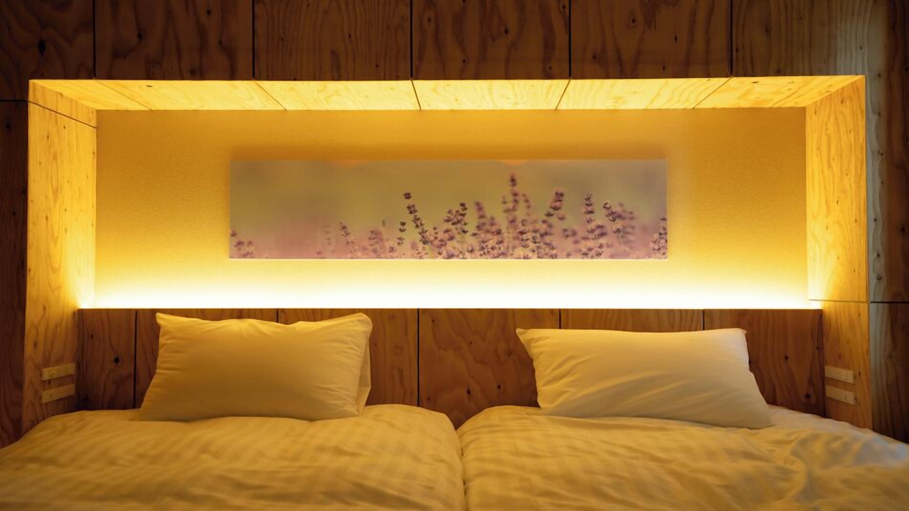 A double bed with two pillows, a wooden headboard, and a wall-mounted light fixture with a floral design.