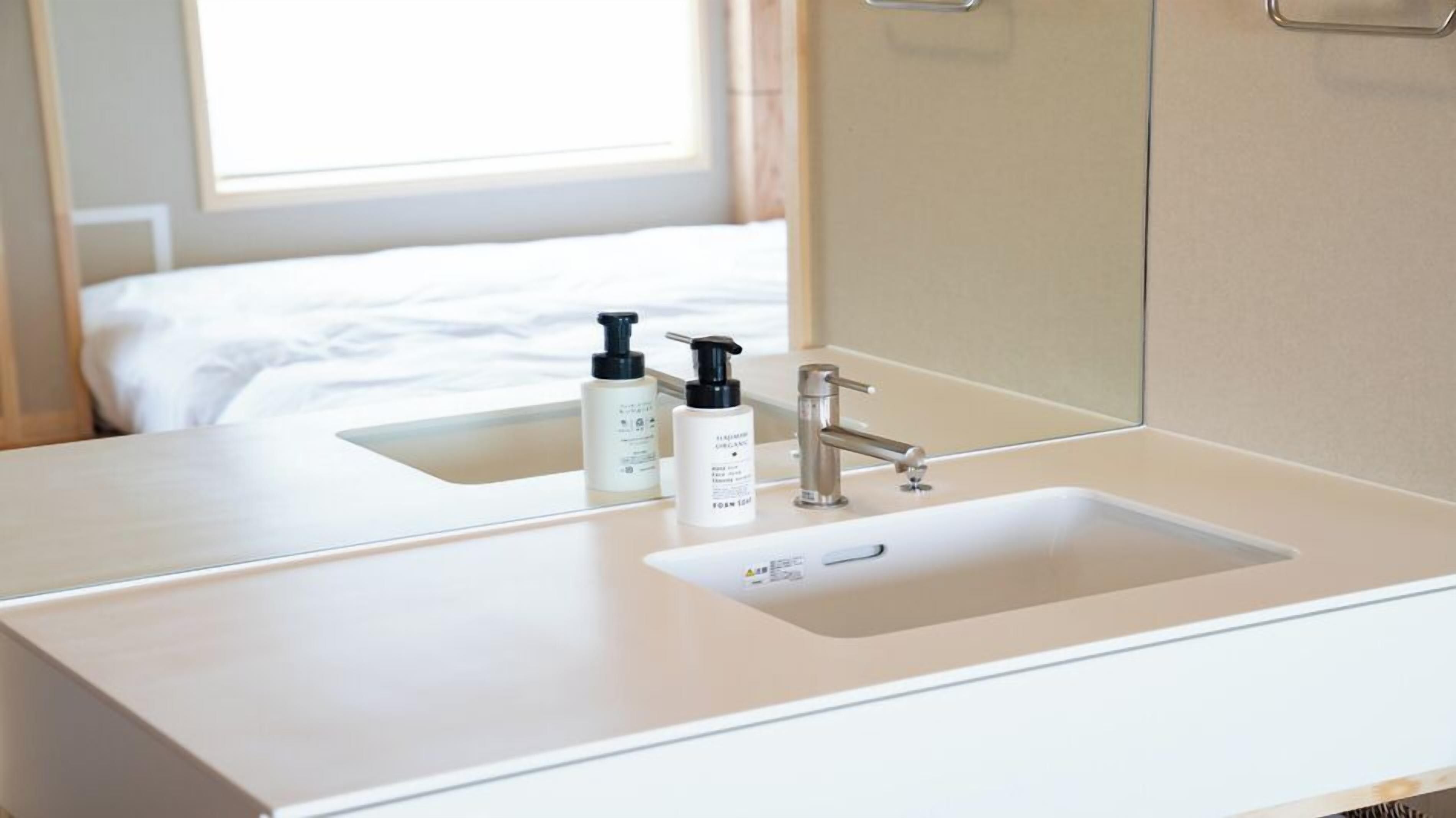 A hotel bathroom with a white sink, a mirror, and two bottles of toiletries.