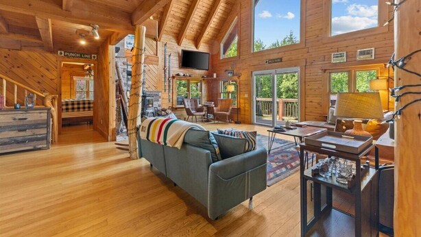 A spacious wooden cabin with a loft bedroom, a living area with a sofa and coffee table, and a dining area with a table and chairs. - Three Peaks Retreat: Pool, Hot Tub & Fireplace (Hyde Park)