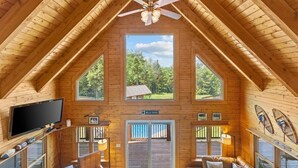 A log cabin with a high ceiling, a ceiling fan, a large TV, and a view of the outdoors. - Three Peaks Retreat: Pool, Hot Tub & Fireplace (Hyde Park)
