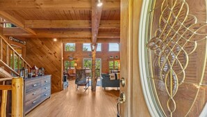 A wooden interior with a staircase, a punch line sign, a wooden door with a decorative glass panel, and a view of the outside through large windows. - Three Peaks Retreat: Pool, Hot Tub & Fireplace (Hyde Park)