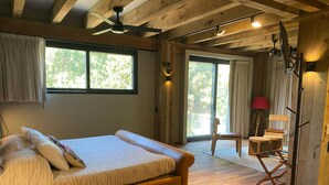 Une chambre à coucher avec un lit, un ventilateur de plafond, une grande fenêtre et une vue sur l’extérieur.